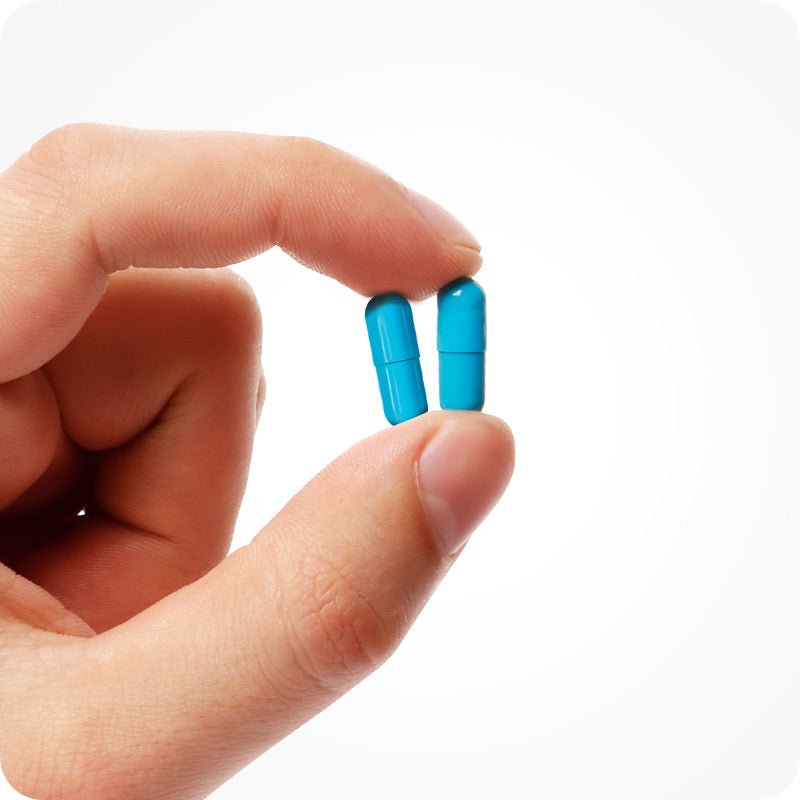 Conceive Plus Men's Fertility Support (IT) capsules shown close-up between two fingers, displaying the size and vibrant blue color of the vegetarian supplements for male fertility health.